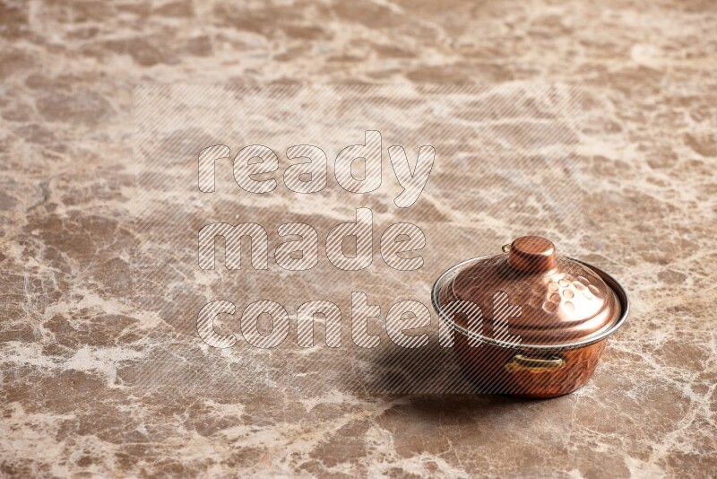A small copper pot on beige marble background