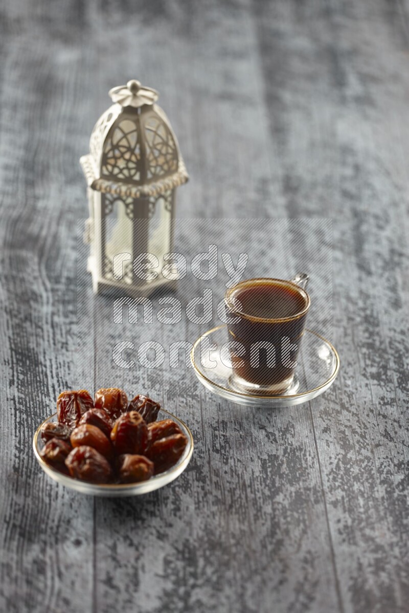A white lantern with different drinks, dates, nuts, prayer beads and quran on grey wooden background