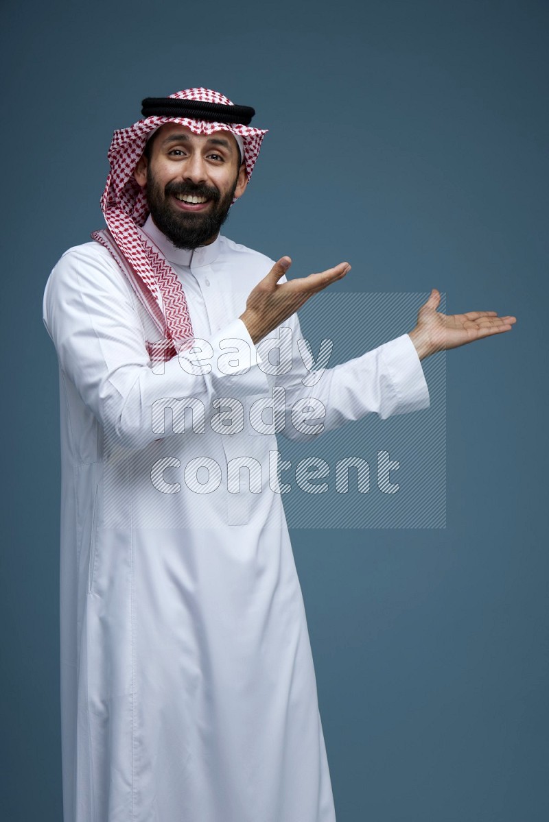 A man pointing in a blue background wearing Saudi Thob and Shomag