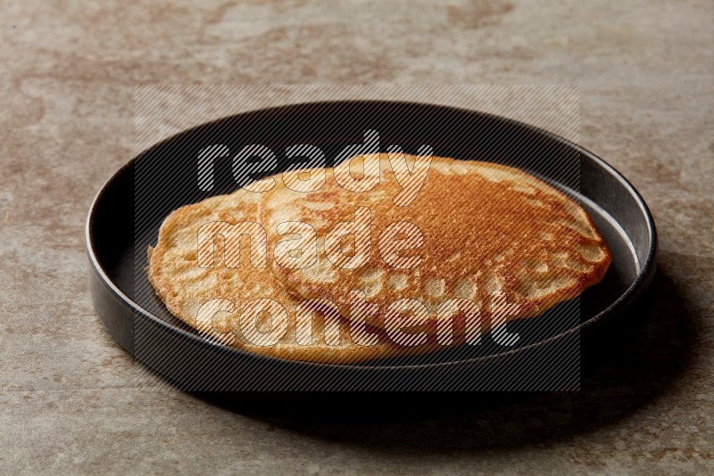 Two stacked plain pancakes in a black plate on beige background