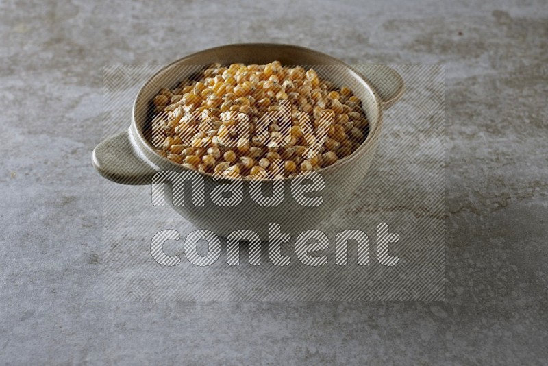corn kernel in a off-white handheld ceramic bowl on a grey textured countertop