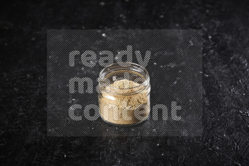 A glass jar full of ground ginger powder on black background