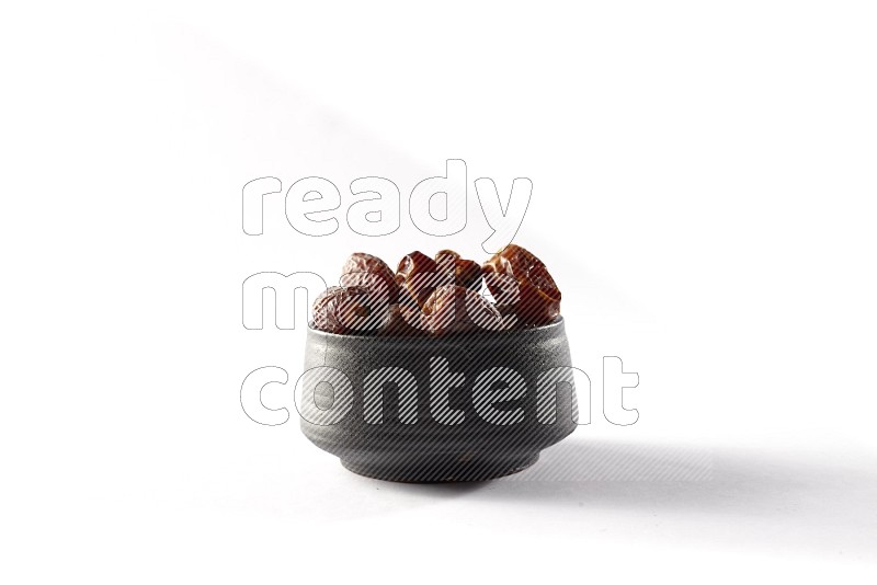 Dates in a black pottery bowl on white background