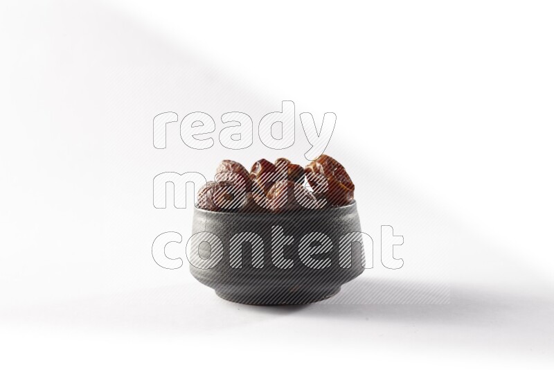 Dates in a black pottery bowl on white background