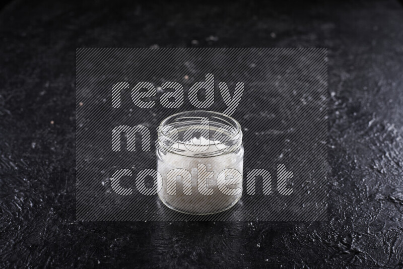 A glass jar full of coarse sea salt crystals on black background