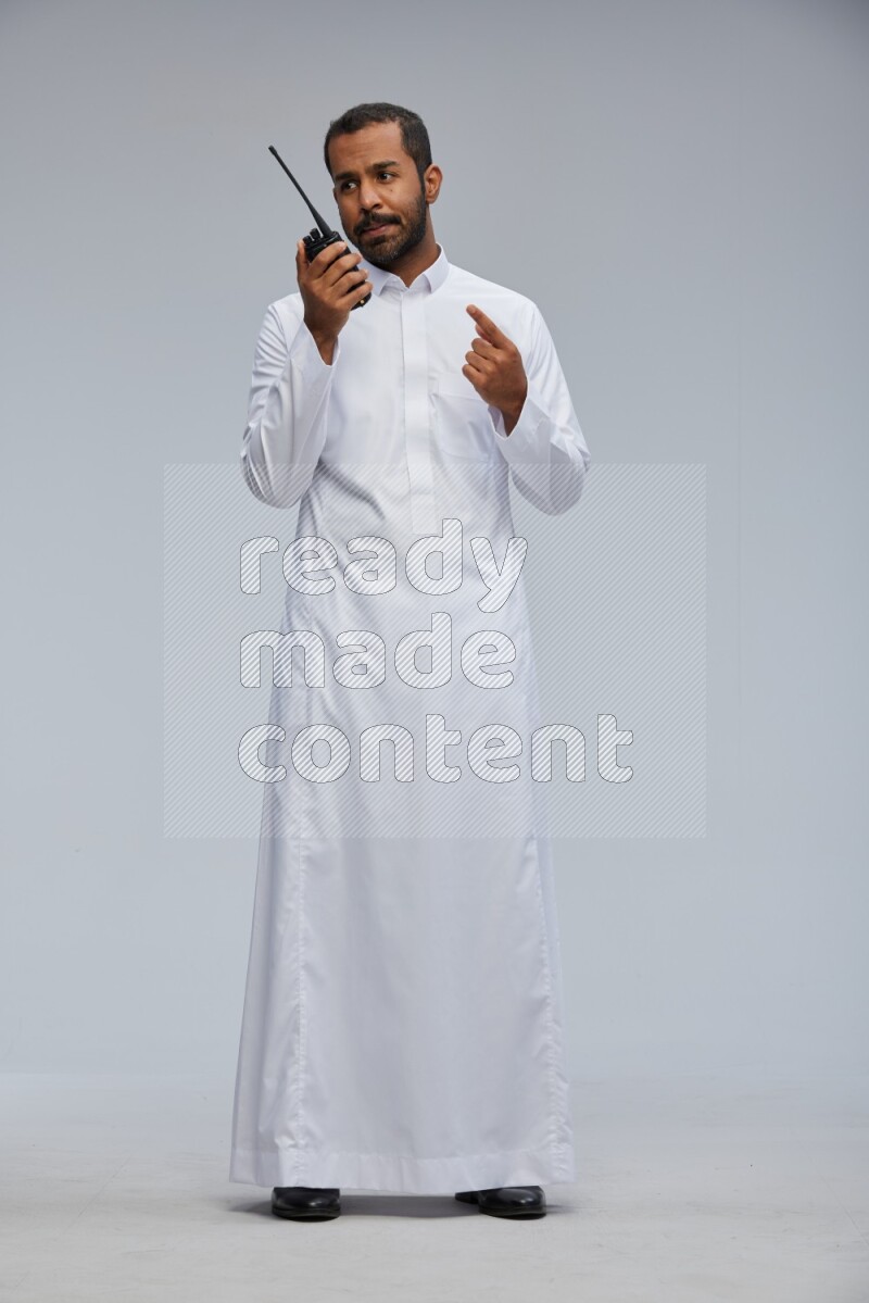 Saudi man Wearing thob standing holding walkie-talkie on Gray background
