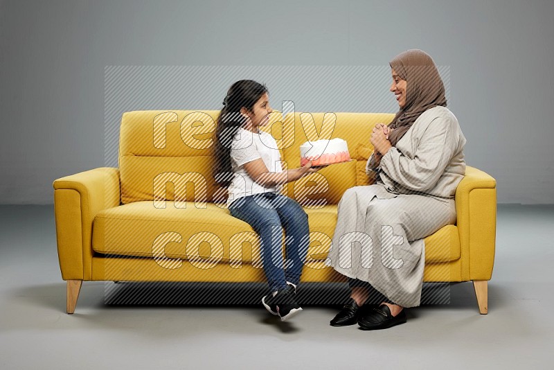 A girl sitting giving a cake to her mother on gray background