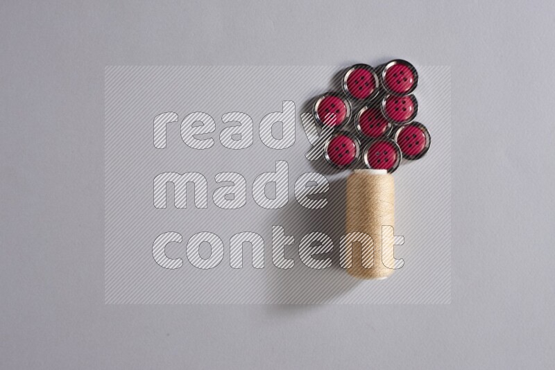 A beige sewing thread spool with colored buttons on grey background