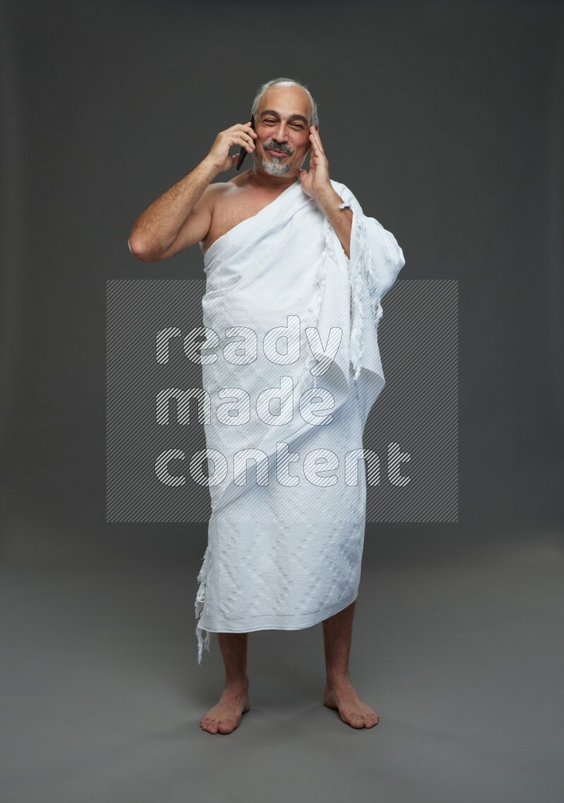 A man wearing Ehram Standing talking on phone on gray background