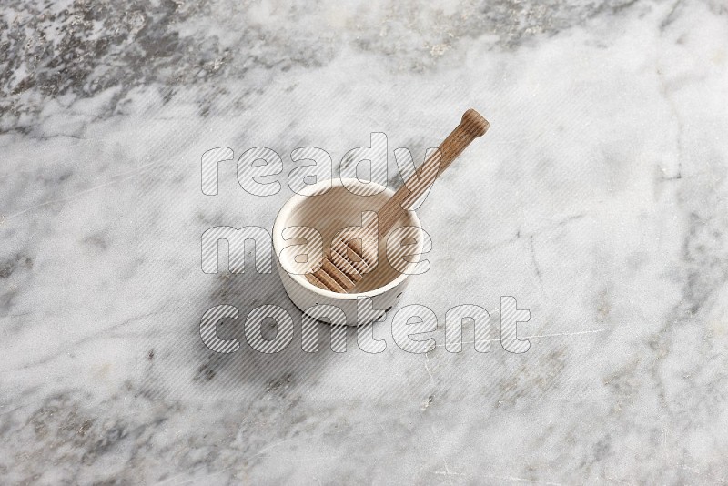White Pottery Bowl with wooden honey handle in it, on grey marble flooring, 65 degree angle