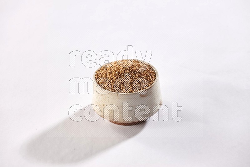 A beige pottery bowl full of mustard seeds on white flooring