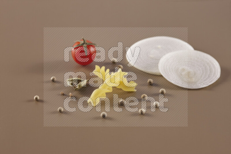 Raw pasta with different ingredients such as cherry tomatoes, garlic, onions, red chilis, black pepper, white pepper, bay laurel leaves, rosemary and cardamom on beige background