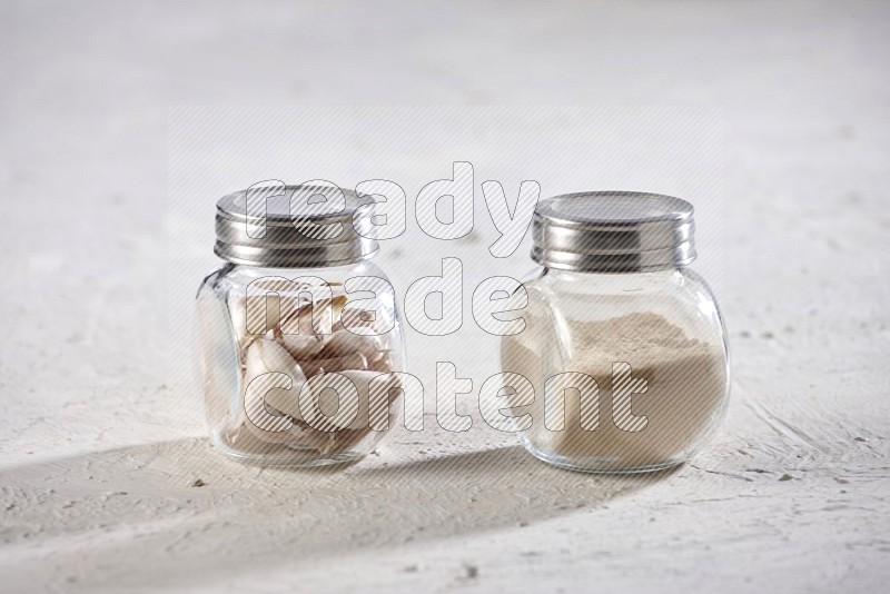 2 glass spice jars full of garlic powder and cloves on a textured white flooring in different angles