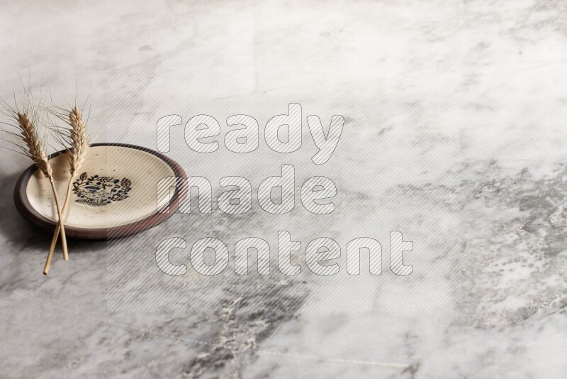 Wheat stalks on decorative pottery plate on grey marble background