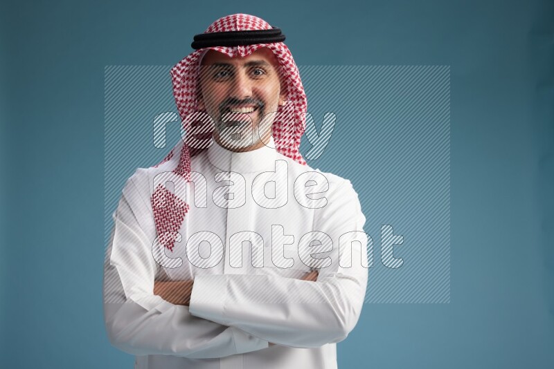 Saudi man wearing thob and shomagh posing to the camera on blue background