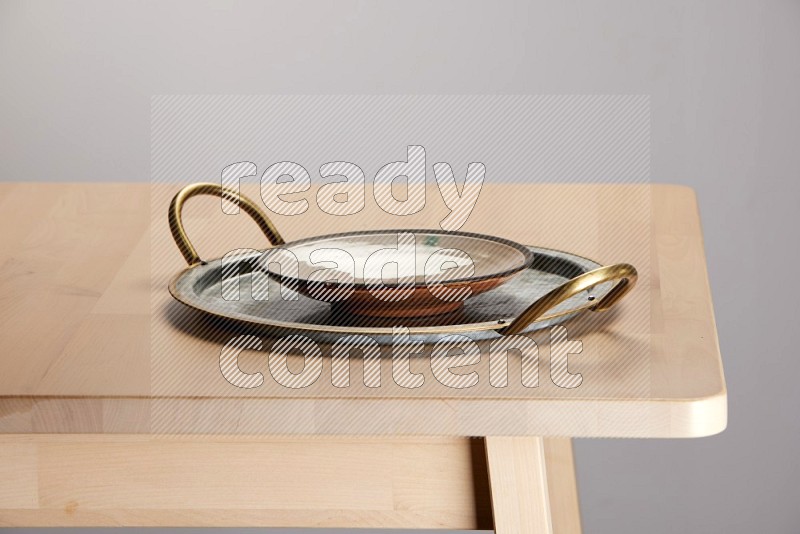 multicolored plate placed on a rounded stainless steel tray with golden handels on the edge of wooden table