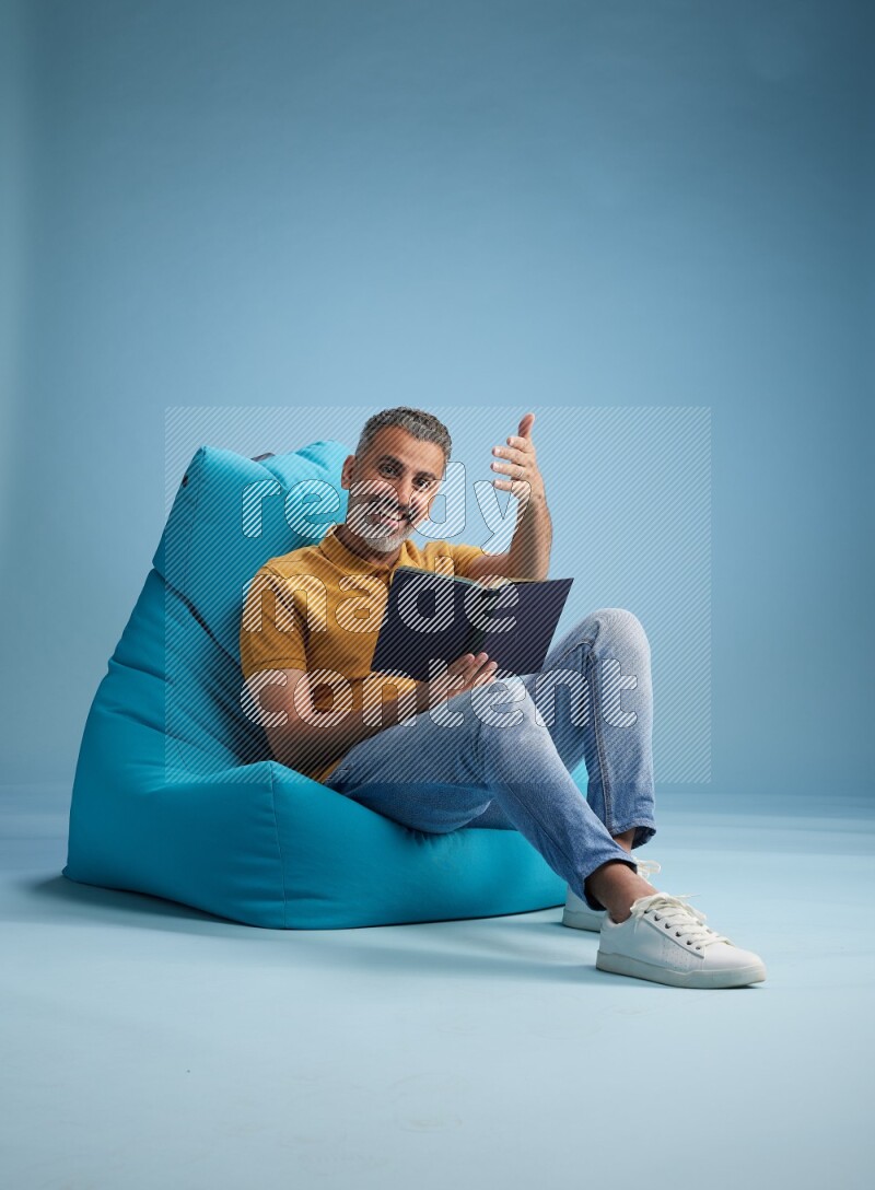 A man sitting on a blue beanbag and reading a book