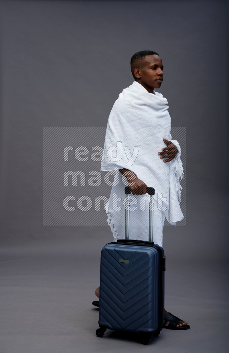 A man wearing Ehram Standing holding traveling bag on gray background