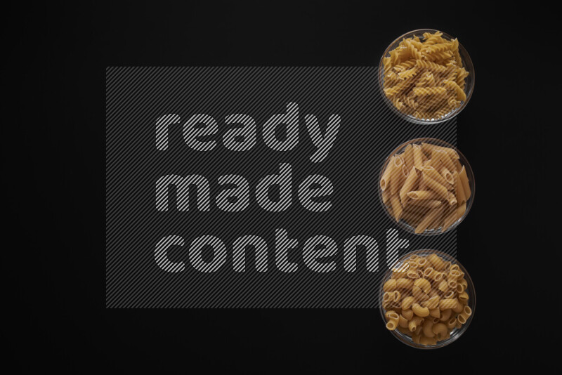 Different pasta types in 3 glass bowls on black background