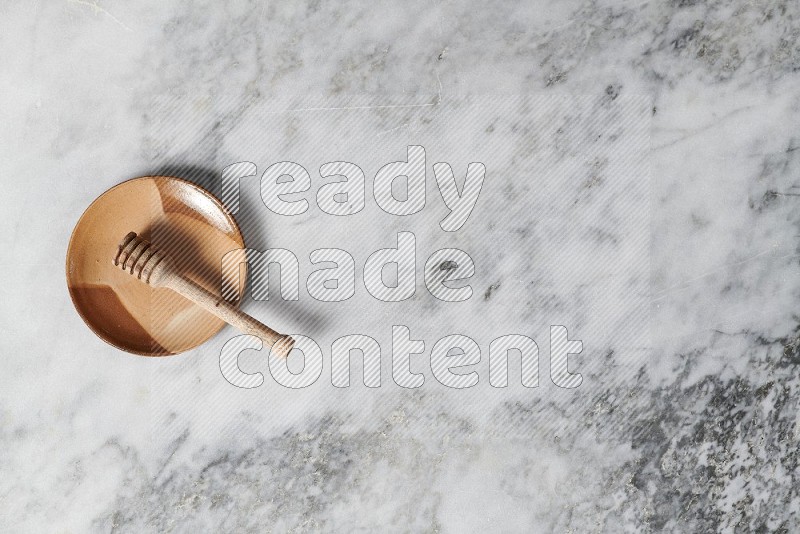 Multicolored Pottery Plate with wooden honey handle in it, on grey marble flooring, Top View