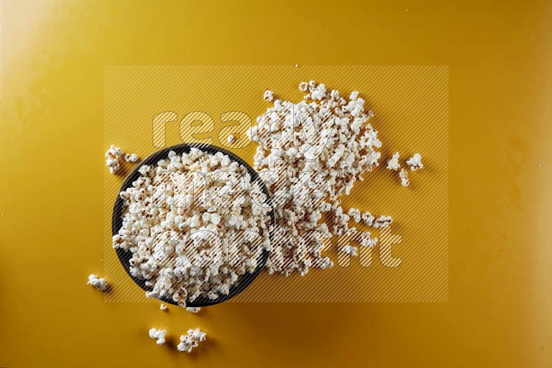 A cooper ceramic bowl full of popcorn with popcorn beside it on a yellow background in different angles