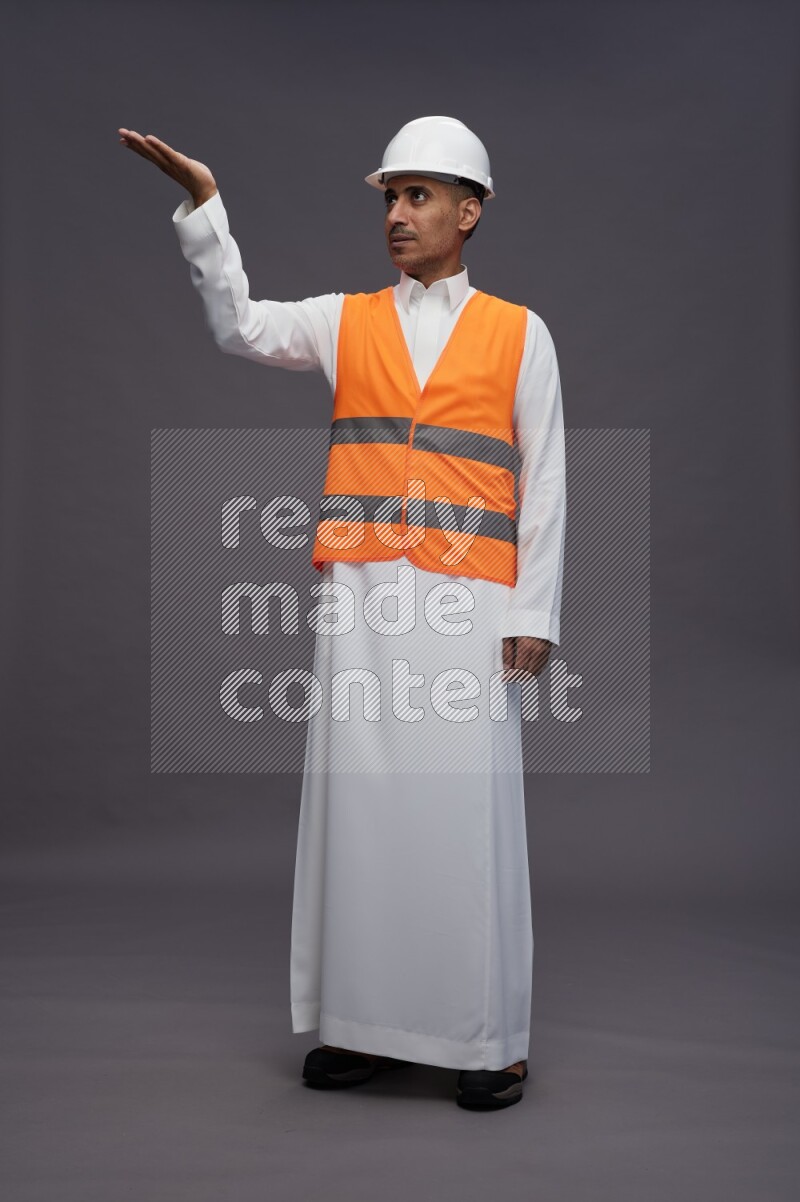 Saudi man wearing thob with engineer vest standing interacting with the camera on gray background