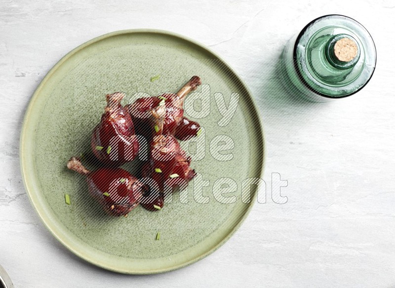 drumstick wrapped in bacon on round light green pottery plate on grey textured countertop
