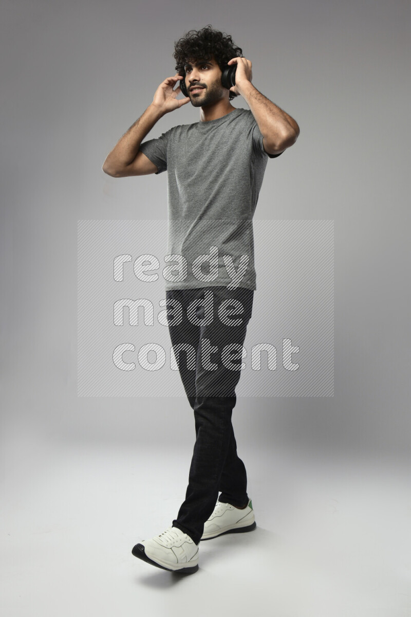 A man wearing casual standing and putting on headphones on white background