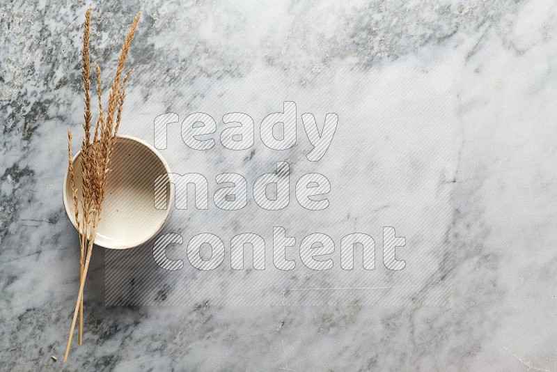 Wheat stalks on Beige Pottery Bowl on grey marble flooring, Top view
