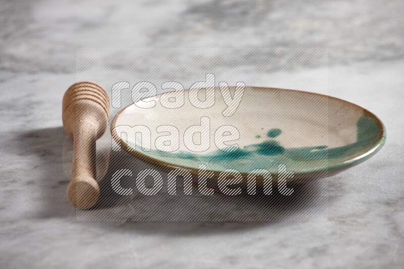 Multicolored pottery plate with wooden honey dipper on the side on grey marble background