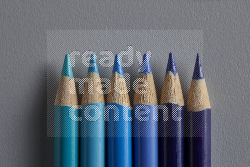 A collection of colored pencils arranged showcasing a gradient of blue hues on grey background