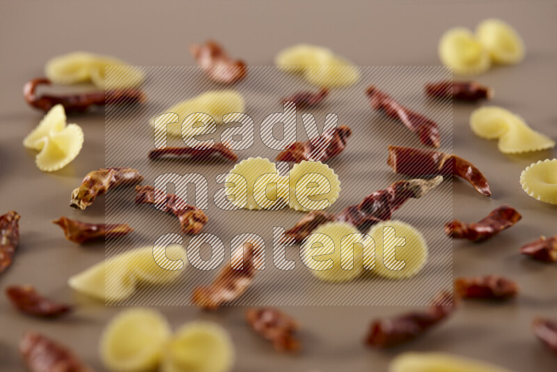 Raw pasta with different ingredients such as cherry tomatoes, garlic, onions, red chilis, black pepper, white pepper, bay laurel leaves, rosemary and cardamom on beige background