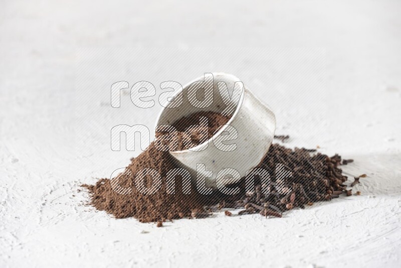 وعاء بيج من السيراميك ممتلئ ببودرة القرنفل وبعض بودرة القرنفل سقطت بخارجه على أرضية بيضاء