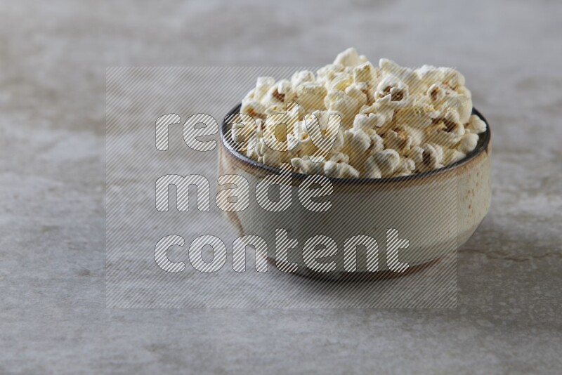popcorn in multi-colored pottery bowl on a grey textured countertop