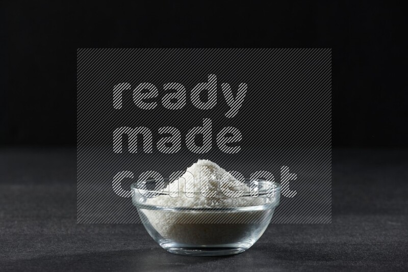 A glass bowl full of desiccated coconut on a black background in different angles