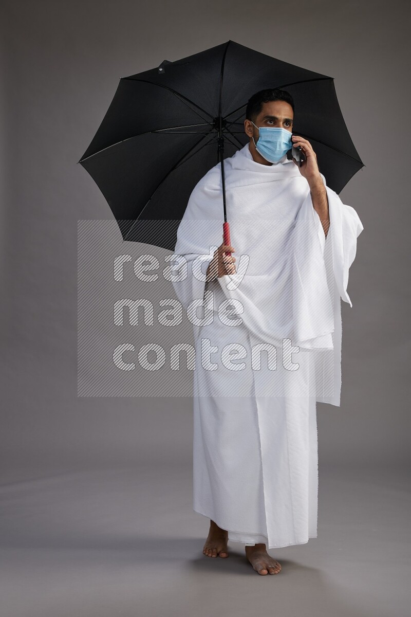 A man wearing Ehram and mask Standing holding umbrella on gray background on gray background