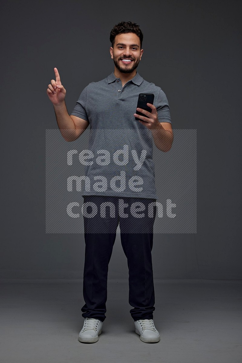 A man wearing casual standing and using his phone and making multi hand gestures eye level on a gray background