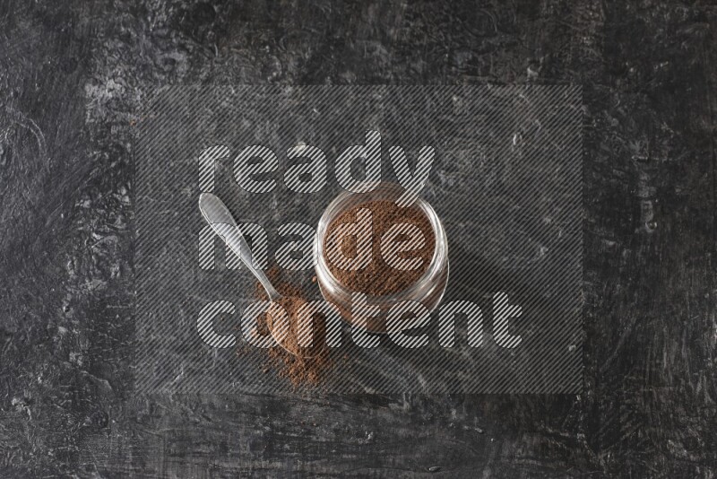 وعاء زجاجي ممتلئ ببودرة القرنفل مع ملعقة معدنية على أرضية سوداء