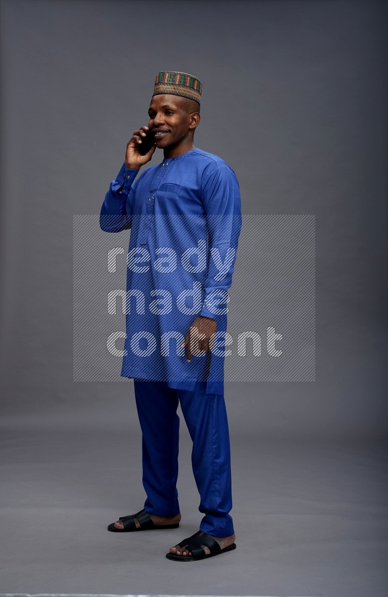 Man wearing Nigerian outfit standing talking on phone on gray background