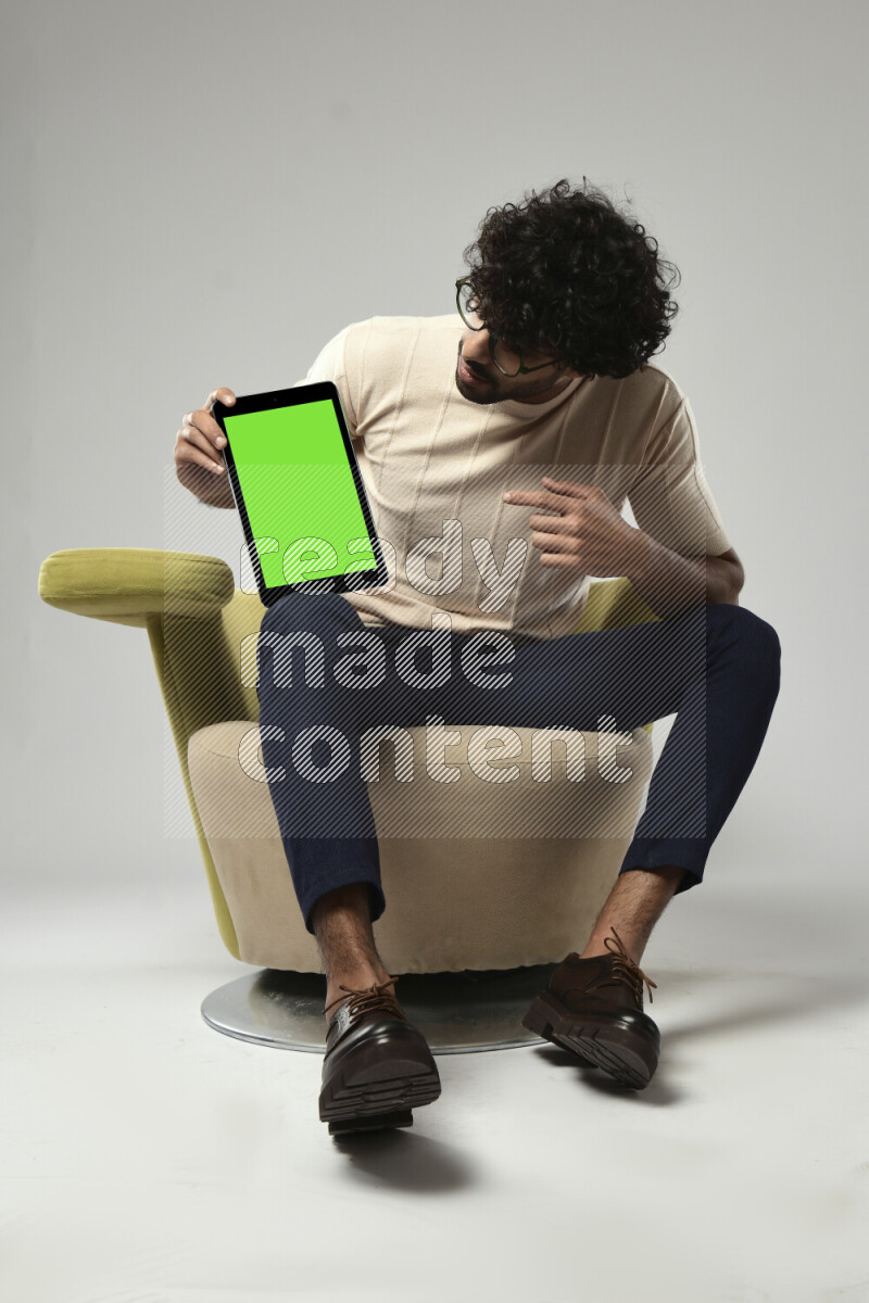 A man wearing casual sitting on a chair showing a tablet screen on white background