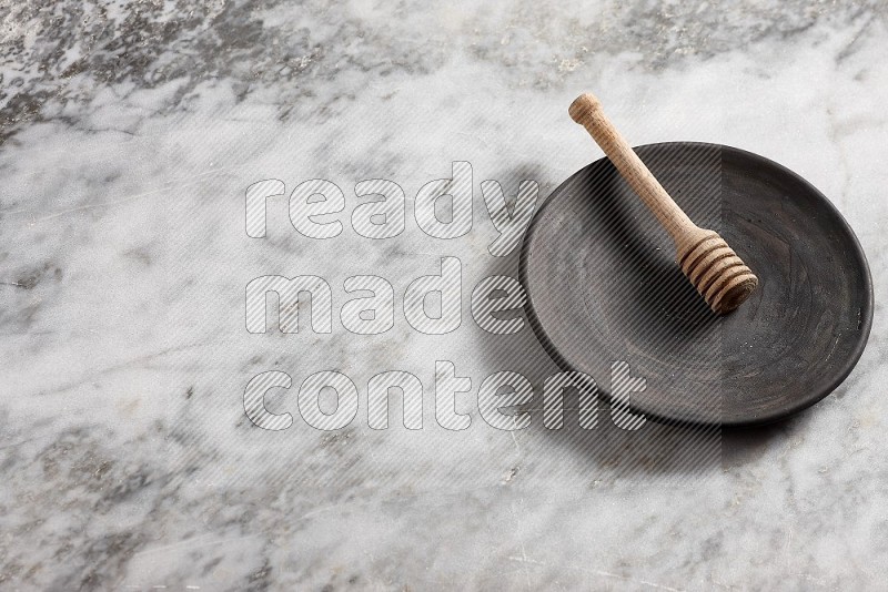 Black Pottery Plate with wooden honey handle in it, on grey marble flooring, 65 degree angle