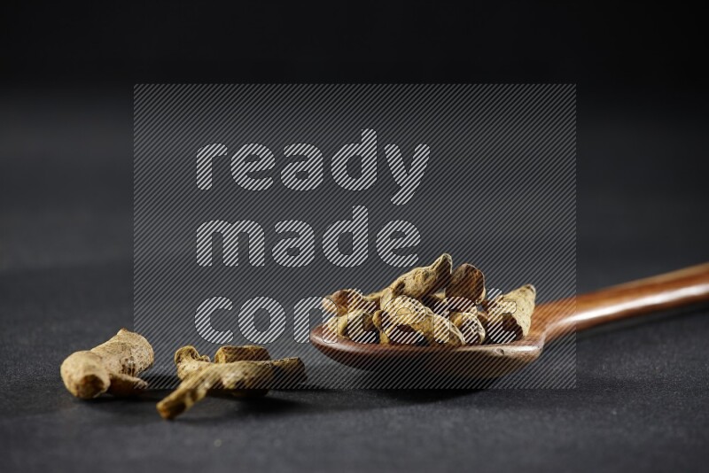 مغرفة خشبية ممتلئة بأصابع الكركم المجففة على خلفية سوداء