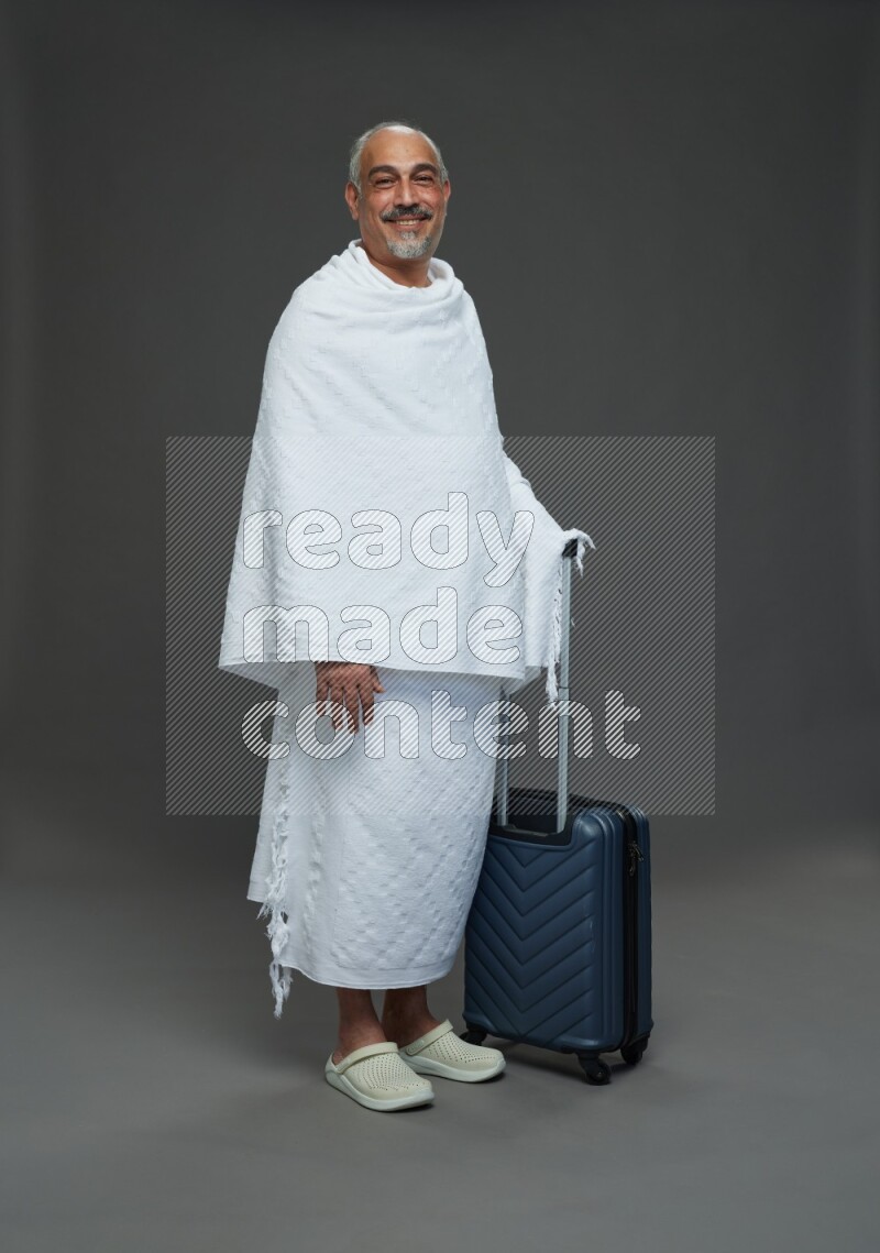 A man wearing Ehram Standing holding traveling bag on gray background