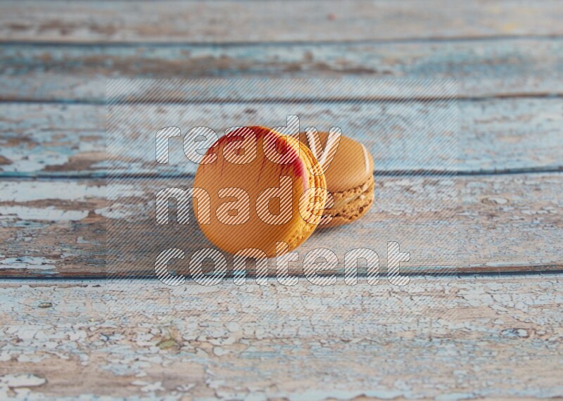 45º Shot of of two assorted Brown Irish Cream, and Orange Exotic macarons on light blue background