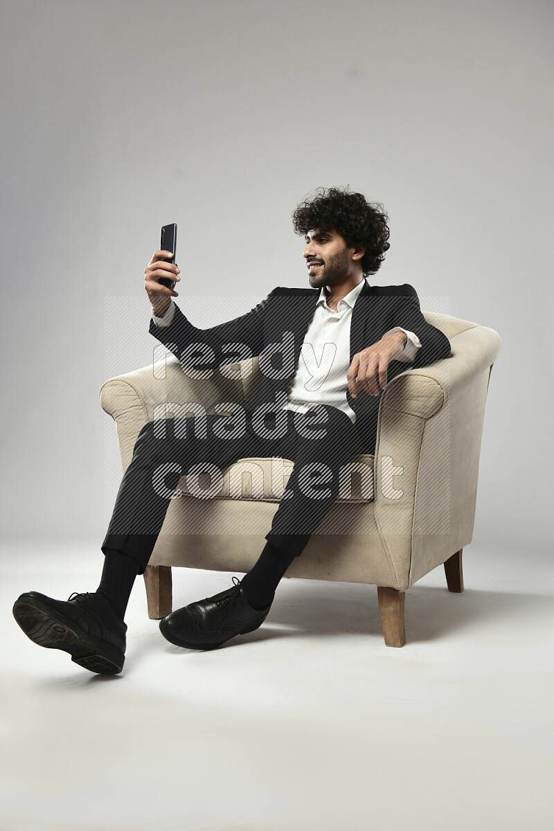 A man wearing formal sitting on a chair taking a selfie on white background