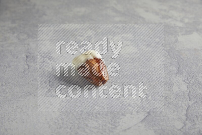 Almond stuffed date coved with white chocolate on a light grey background