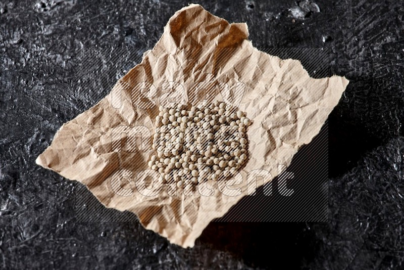 White pepper beads in a crumpled piece of on textured black flooring