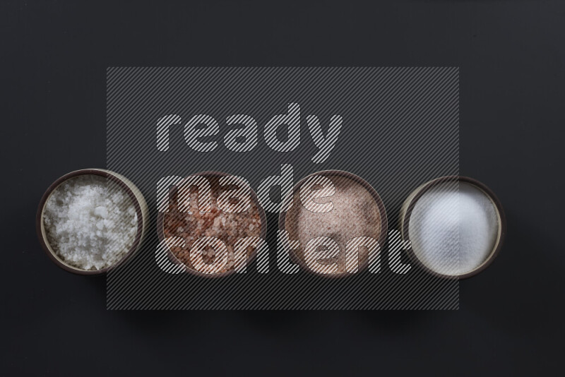 4 pottery bowls filled with himalayan salt and white salt on black background