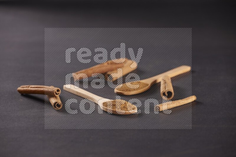 ملعقتان خشبيتان ممتلئتان ببودرة القرفة مع أعواد القرفة على خلفية سوداء