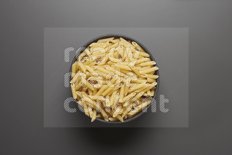 Mini penne pasta in a pottery bowl on grey background